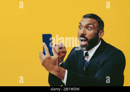 portrait d'un homme barbu enragé en costume et cravate avec appel vidéo smartphone pointant le doigt vers l'arrière-plan jaune de l'appareil photo Banque D'Images