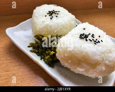 2 boulettes de riz japonaises Onigiri avec Kuro Goma (sésame) et Takana (Takana-zuke, vert moutarde japonais mariné) sur une assiette. Banque D'Images