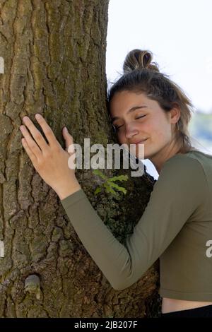 Une jeune femme contentée embrasse un grand arbre avec une expression blissful et ses yeux fermés dans un concept de sauver la forêt, d'arrêter la déforestation, le jour de la terre, en lien avec la nature et la conservation de la nature. Photo de haute qualité Banque D'Images