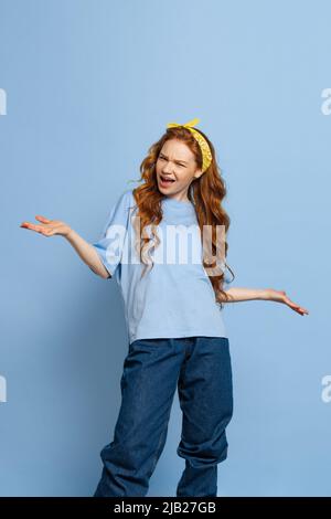 Agacé jeune fille à tête rouge, étudiant posant isolé sur fond de studio bleu. Émotions humaines, concept d'expression faciale. Couleurs tendance Banque D'Images