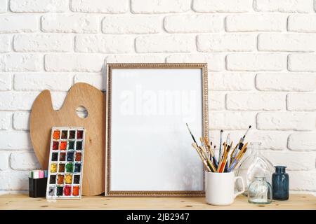 Cadre photo comme chevalet avec les outils de l'artiste sur une table en bois contre un mur en brique blanche Banque D'Images