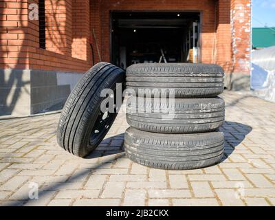 Un nouvel ensemble de pneus d'été empilés sur le trottoir dans la cour. Les pneus de voiture sur les jantes en acier sont prêts pour le remplacement saisonnier. Banque D'Images