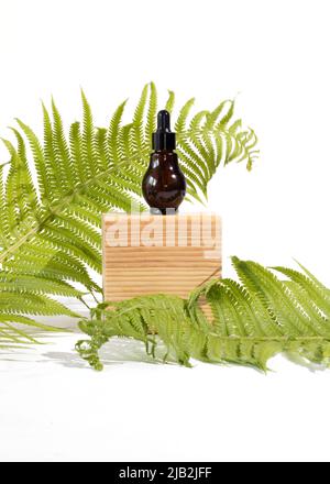 Flacon de sérum en verre ambré avec une pipette sur un podium en bois sur fond de fougères. Concept de cosmétiques naturels biologiques. Banque D'Images