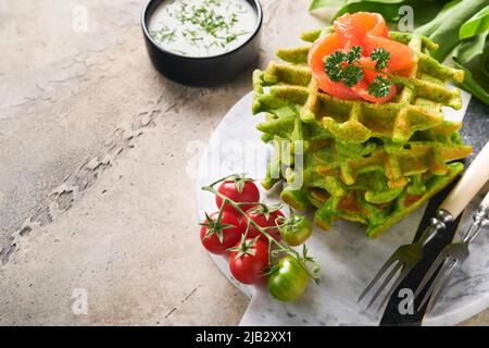 Gaufres belges vertes. Épinards ou ail sauvage ou gaufres au pesto avec saumon rouge et sauce à la crème sur fond de table en béton gris. Délicieux petit déjeuner, Banque D'Images