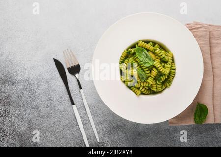 Pâtes italiennes Fusilli au pesto. Pâtes fusilli au pesto de basilic et aux herbes, parmesan, basilic et ail sur plaque blanche sur comptoir en pierre grise Banque D'Images