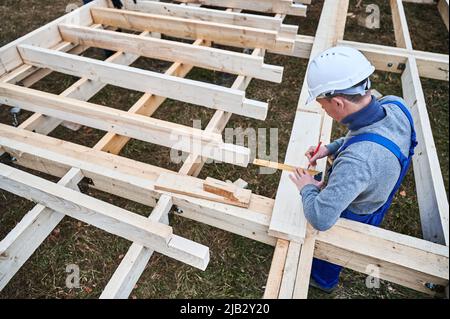 Homme ouvrier bâtiment maison de cadre en bois sur la base de pile. Menuisier utilisant l'angle pour mesurer des planches en bois et faire des marques avec un crayon. Concept de menuiserie. Banque D'Images