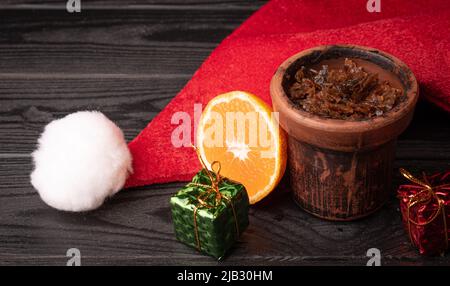 Bol à narguilé avec tabac et chapeau rouge de Noël sur fond sombre. Accessoires de Noël Banque D'Images