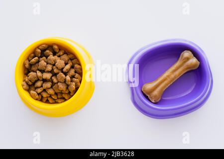 vue de dessus des friandises en forme d'os pour animaux dans un bol près de la nourriture sèche pour animaux isolée sur blanc Banque D'Images