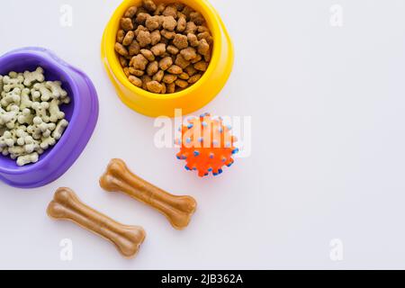 vue de dessus des biscuits pour animaux en forme d'os et de la nourriture sèche dans les bols près de la boule de caoutchouc isolée sur blanc Banque D'Images