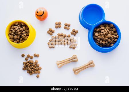 vue de dessus de la forme de patte faite de nourriture sèche pour animaux près des os et des bols isolés sur blanc Banque D'Images