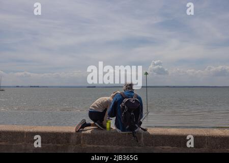 Southend on Sea, Royaume-Uni. 2 juin 2022. Deux voyageurs sont assis sur un mur de mer en pierre surplombant un horizon côtier calme, vêtus de vêtements de plein air et de sacs à dos. Une flèche verte suggère un itinéraire ou un sentier pédestre. La scène évoque un moment de repos et de réflexion lors d’un voyage le long de la côte britannique. Les touristes viennent à Southend on Sea pour la journée pour profiter du jour férié et profiter du temps chaud. Penelope Barritt/Alamy Live News Banque D'Images