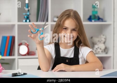 bonne fille tient des ciseaux dans la salle de classe de l'école Banque D'Images