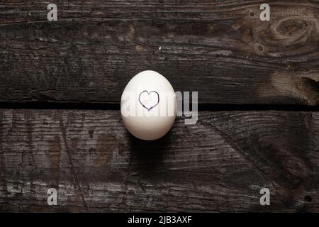 le coeur est tiré sur un œuf de poulet qui se trouve sur une vieille table en bois, l'amour et les sentiments Banque D'Images