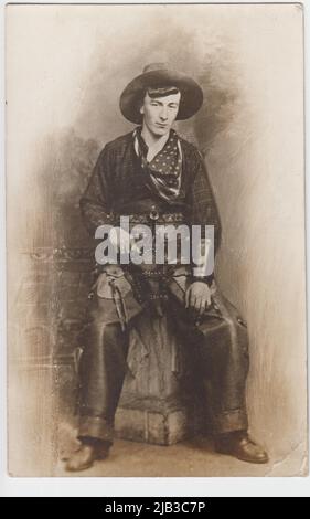 Portrait de studio d'un cow-boy, avec chapeau de cow-boy, bandana drapeau américain, chemise à carreaux, fusil dans l'étui et pantalon en cuir. Il pourrait montrer un interprète dans l'un des spectacles du Wild West qui a visité le Royaume-Uni au début du 20th siècle Banque D'Images