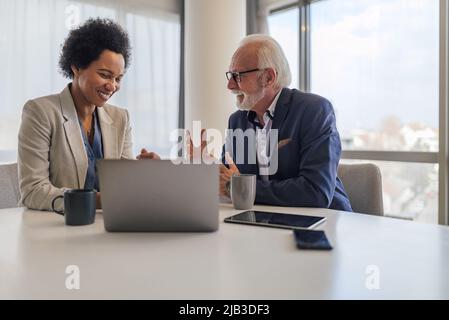 Homme d'affaires senior discutant avec la direction féminine. Des professionnels souriants, hommes et femmes, planifient une stratégie pendant la réunion. Ils sont assis à o Banque D'Images