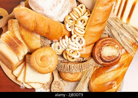 Arrière-plan culinaire avec pain, petits pains, bagels de séchage, oreilles de blé, grains dans un panier en osier, sur une table en bois vue. Banque D'Images