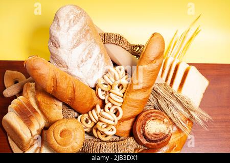 Arrière-plan culinaire avec pain, petits pains, bagels de séchage, oreilles de blé, grains dans un panier en osier, sur une table en bois vue. Banque D'Images