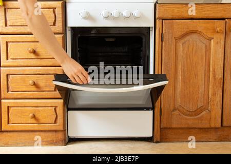 Cuisinière à gaz intégrée et armoires de cuisine en bois dans la cuisine, cuisinière à gaz, une femme ouvre à la main le four dans la cuisine Banque D'Images