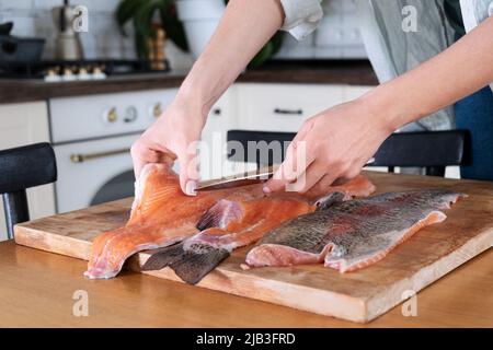 Les mains de femmes coupant le filet de poisson rouge. Caviar rouge. Retrait des os de poisson. Concept alimentaire. Cuisine du poisson dans la cuisine à la maison Banque D'Images