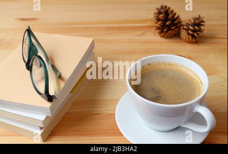 Une tasse de café chaud mousseux avec une pile de livres et de lunettes sur une table en bois Banque D'Images