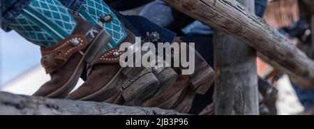 Bottes de cowboy et éperons assis sur la clôture du corral en regardant un rodéo Banque D'Images