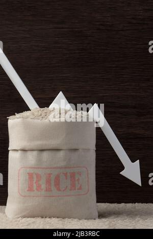 Récolte de riz. Mauvaises récoltes agricoles, pénuries alimentaires, faim dans le monde. Un sac de riz sur fond marron avec une flèche blanche pointant vers le bas. Banque D'Images