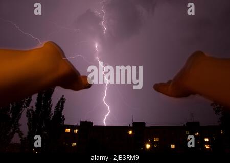 Les mains des femmes sont étirées vers le ciel sur fond de foudre au-dessus de la ville et des maisons la nuit, une prière à Dieu pendant un orage, Banque D'Images