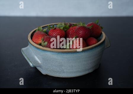 Bol de framboises dans un bol en céramique bleu fait à la main sur fond sombre avec un mur en béton gris. Banque D'Images