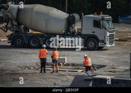 Une œuvre féminine méconnaissable et deux ouvriers masculins méconnaissables discutent de problèmes sur le chantier de construction, un camion de transport en béton en arrière-plan Banque D'Images