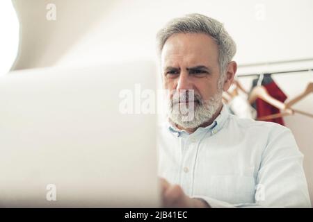 Concept d'entreprise familiale. Homme d'affaires d'âge moyen dans son studio travaillant sur un nouveau projet. Regardez l'écran de votre ordinateur portable. . Photo de haute qualité Banque D'Images