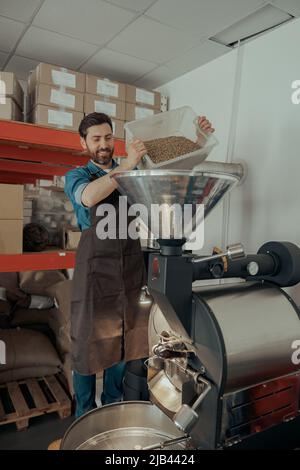 Entrepreneur verse des grains de café crus dans une machine à rôtir moderne. Banque D'Images