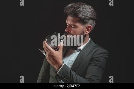 Homme barbu en costume noir et verre de whisky en loft. Homme plein de confiance et bien habillé avec un verre de whisky. Banque D'Images