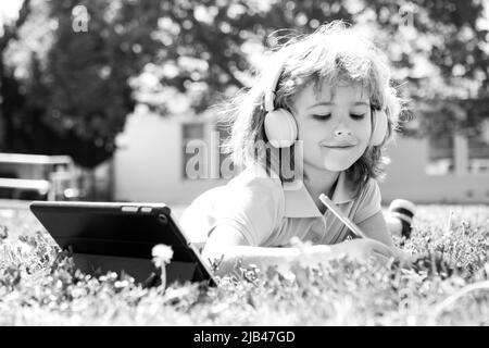 Un petit élève utilise un ordinateur portable ou une tablette et écrit du nomwork dans le parc scolaire. Enfant scolaire en bonne santé. Banque D'Images