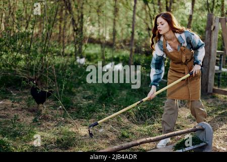 Une femme paysanne nettoie la plume de volaille avec le râteau pour maintenir l'ordre et les soins pour les poulets sur la ferme extérieure Banque D'Images