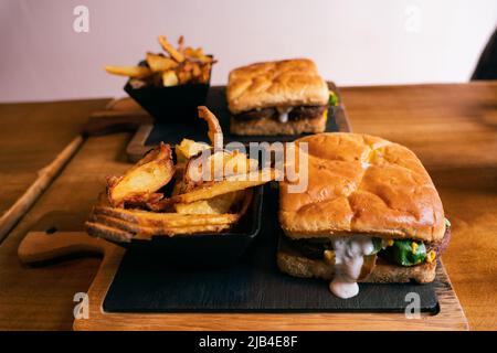 Délicieux sandwich ou hamburger avec une portion de frites de pommes de terre dorées sur un panneau sombre en bois Banque D'Images