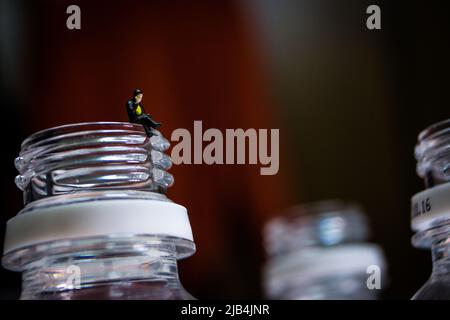 Homme d'affaires miniature assis sur le cou de la bouteille en plastique. L'homme en image passe un appel téléphonique avec son téléphone mobile. Banque D'Images