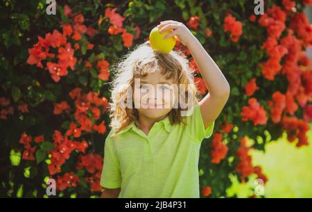 Petit enfant avec pomme rouge sur la tête à l'extérieur. Banque D'Images