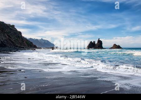 Plage de sable volcanique noir - Beniho, les vagues de l'océan s'écoulent doucement vers la rive, d'énormes falaises rocheuses dans l'océan Banque D'Images