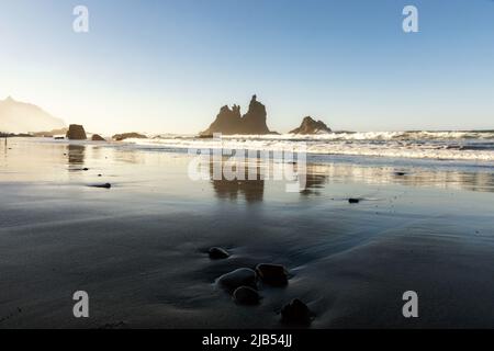 Plage de sable volcanique noir - Beniho, les vagues de l'océan s'écoulent doucement vers la rive, d'énormes falaises rocheuses dans l'océan Banque D'Images