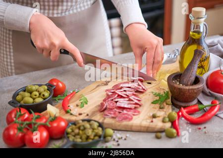 Femme trancheuse de salami de fuet de saucisse espagnole avec un couteau sur une cuisine domestique Banque D'Images