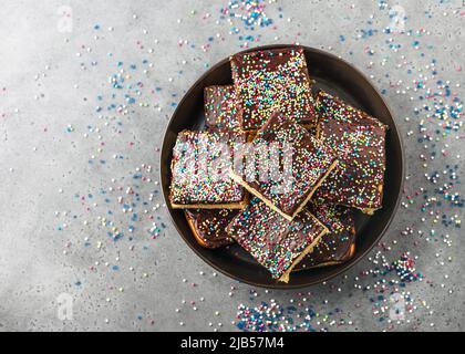 Gâteau fait maison recouvert de glaçage au chocolat et de saupoudrage coloré dans des barres sur l'assiette pour l'anniversaire ou la fête. Vue de dessus. Copier l'espace. Banque D'Images