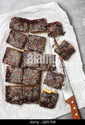 Délicieux gâteau au biscuit avec glaçage au chocolat noir et sucre coloré parsemé de barres sur papier à pâtisserie avec couteau. Concept de mets sucrés maison. Vue de dessus Banque D'Images