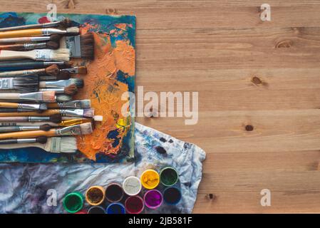 Collection de pinceaux de différentes tailles sur une ancienne palette avec des couleurs de peinture à l'huile se mélangent et un ensemble de gouache, vue de dessus Banque D'Images