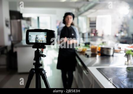 Cuisinez en toute confiance en tournant un vlog culinaire pour une plate-forme en ligne et un programme de télévision. Chef souriant devant l'appareil photo tout en filmant un cours de cuisine dans la cuisine professionnelle du restaurant. Banque D'Images