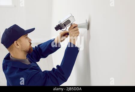 Un technicien professionnel répare ou installe un système de caméra de vidéosurveillance sur un mur à l'intérieur de la maison. Banque D'Images