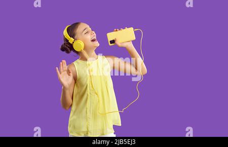 Insouciante, la jeune fille de la préadolescence dans le casque chante la chanson préférée et utilise le téléphone mobile comme microphone. Banque D'Images