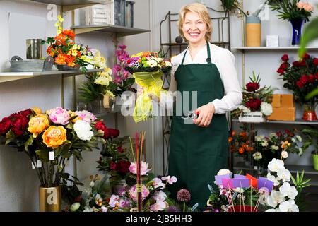 Fleuriste en tablier tenant des ciseaux et fixant des fleurs Banque D'Images