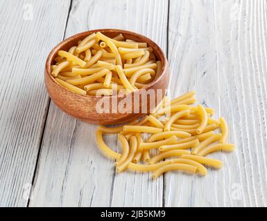 Pâtes de maccheroni non cuites dans un bol en bois sur fond de bois blanc Banque D'Images