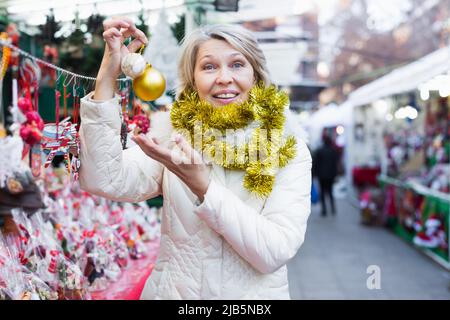 Bonne femme mûre en guirlande avec des jouets de Noël à la foire Banque D'Images