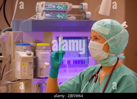 Une infirmière de théâtre d'anesthésie est vue dans un théâtre d'opération. Elle est vue vêtue de vêtements médicaux verts stériles avec un masque facial sur son visage. Banque D'Images